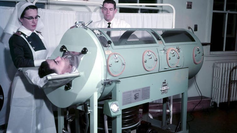 A nurse stands next to man in an iron lung