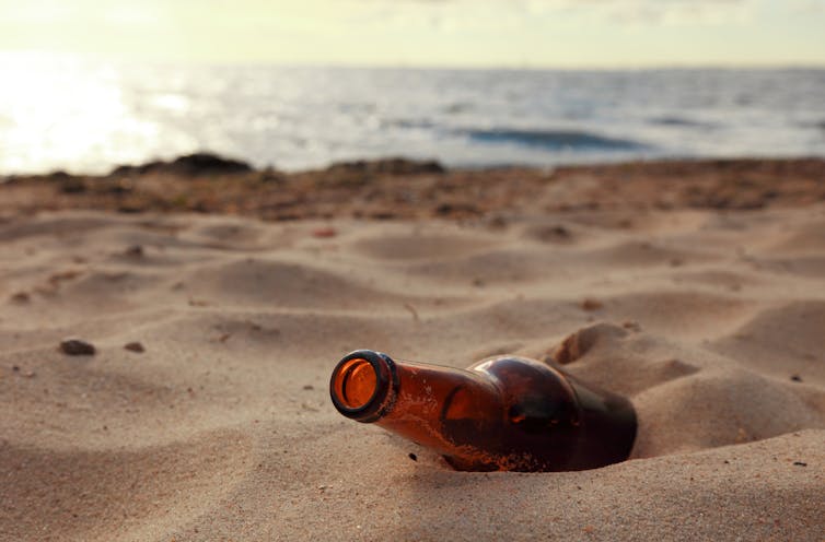 An empty beer bottle on a sandy beach.