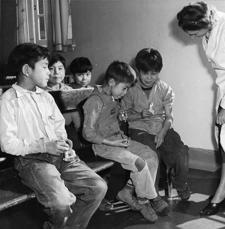 A nurse watches as boys spit into test tubes