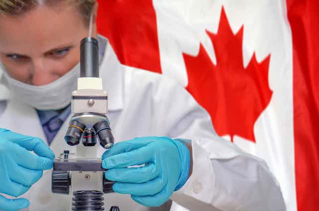 A woman scientist uses a microscope as the Canadian flag waves in the background