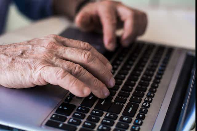 Wrinkled hands on a laptop keyboard.