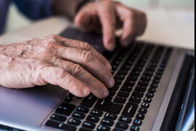 Wrinkled hands on a laptop keyboard.