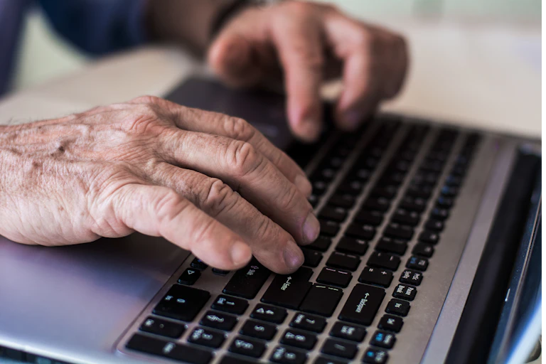 Wrinkled hands on a laptop keyboard.