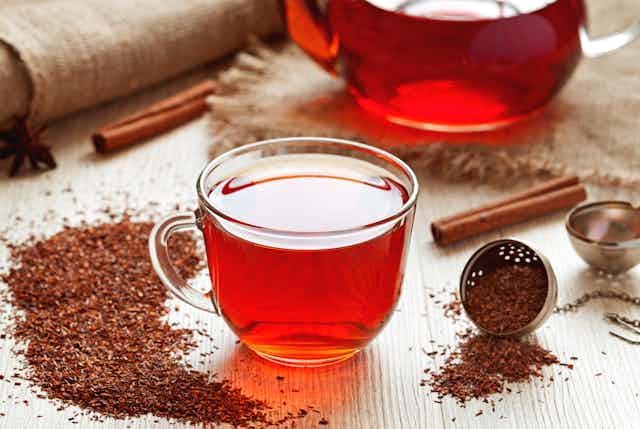 A cup of rooibos tea on a table, surrounded by loose tea, a teapot and spices