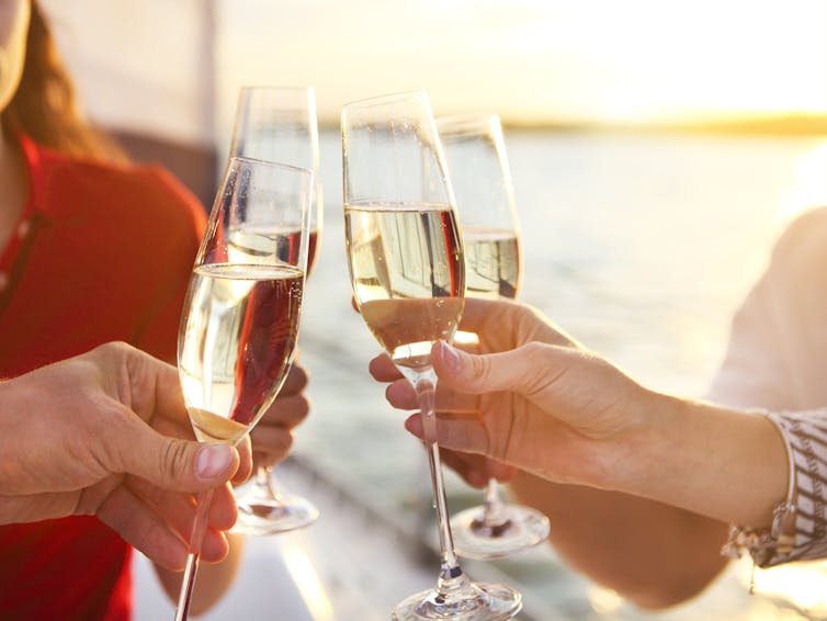 Four people clinking glasses of champagne in front of a sunset