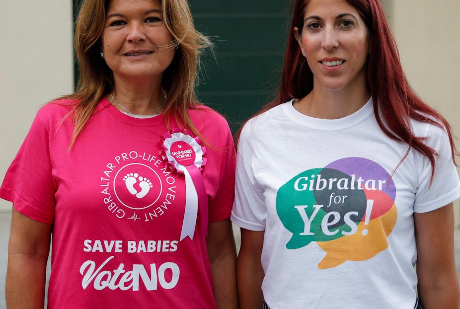 Two women standing side by side, one with a t-shirt reading "save babies vote no," the other with a shirt reading "Gibraltar for yes"