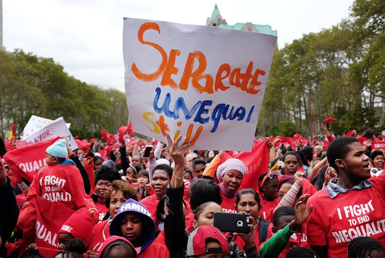 A rally of students and families wearing red T-shirts that say 'I fight to end equality'