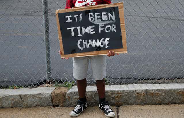 Child holds painted sign that says 'It's been time for change'