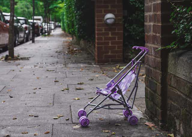 A purple stroller without a child on a sidewalk.