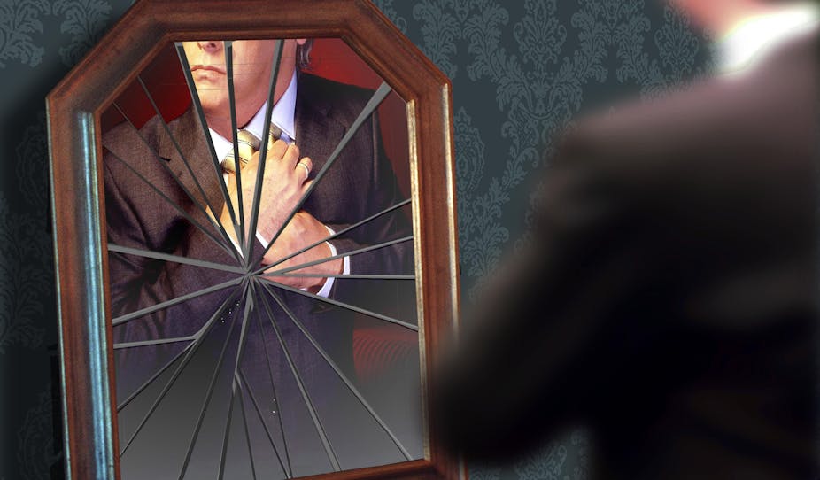 A man adjusts his tie in a broken mirror.