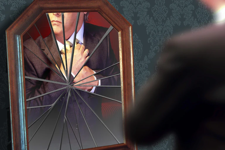 A man adjusts his tie in a broken mirror.