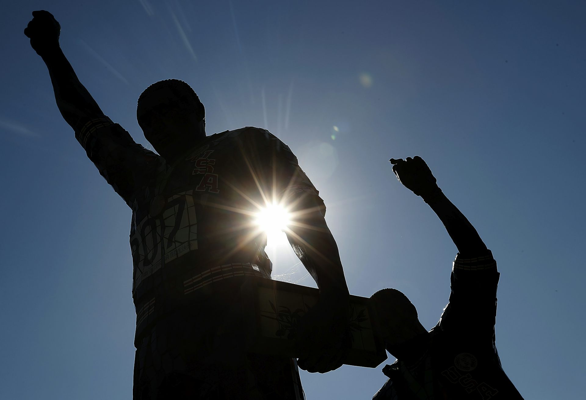 Statues of two men with raised fists are in silhouette 