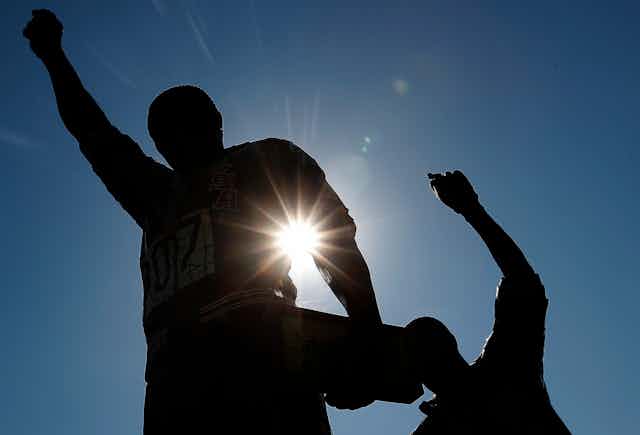 Statues of two men with raised fists are in silhouette