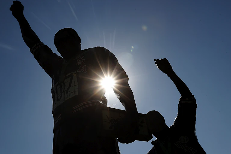 Statues of two men with raised fists are in silhouette