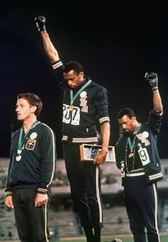Two athletes with fists raised in protest standing on Olympic podium.