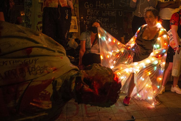 A woman dances next to a toppled statue of Egerton Ryerson.