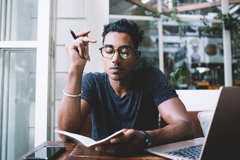 A young man sitting by a window with a pen and paper.