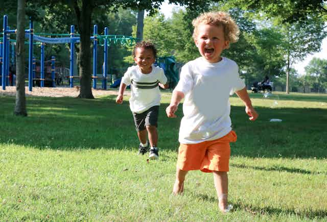 Two young children run outside near a playground.