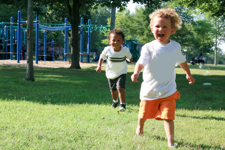 Two young children run outside near a playground.