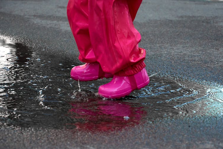 A child's feet in a rainsuit and rainboots jump in a puddle.