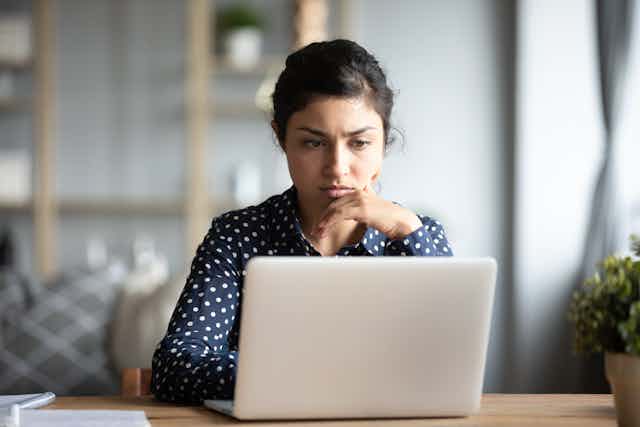 Young woman sitting at a table looks at a computer screen with a concerned expression.