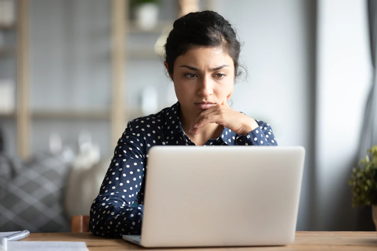 Young woman sitting at a table looks at a computer screen with a concerned expression.