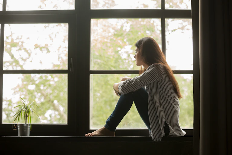 A woman sits in front of a woman, looking out sadly.