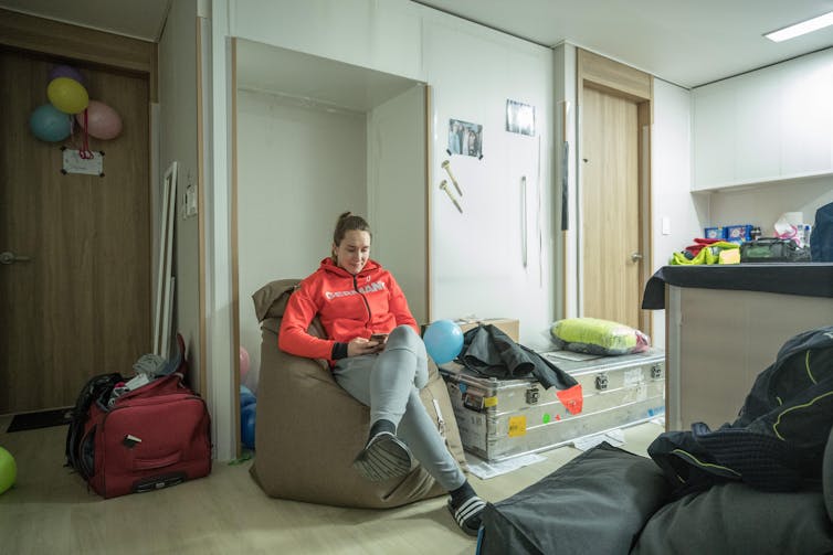 A girl in a red hoodie sits on a giant beanbag in a small hotel room minimally decorated with balloons