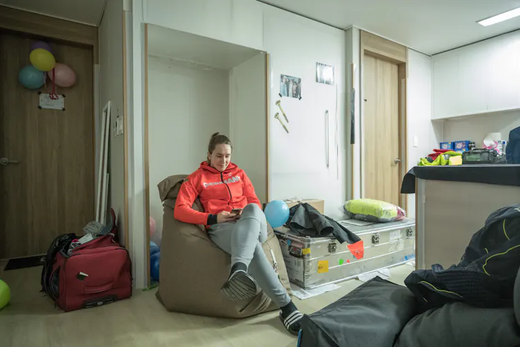 A girl in a red hoodie sits on a giant beanbag in a small hotel room minimally decorated with balloons