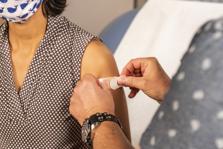 Health worker putting a bandaid on a person's arm after vaccination.