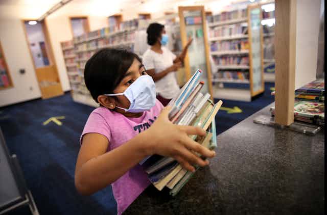 Girls wearing mask holds stack of books
