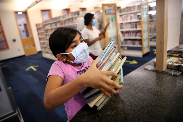 Girls wearing mask holds stack of books
