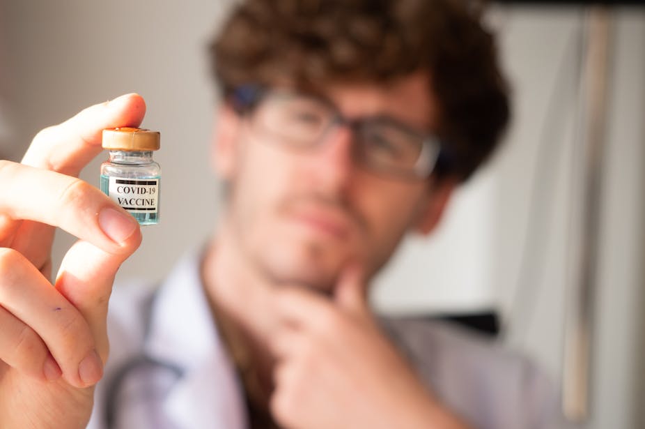 A man looks quizzically at a phial of COVID-19 vaccine. 