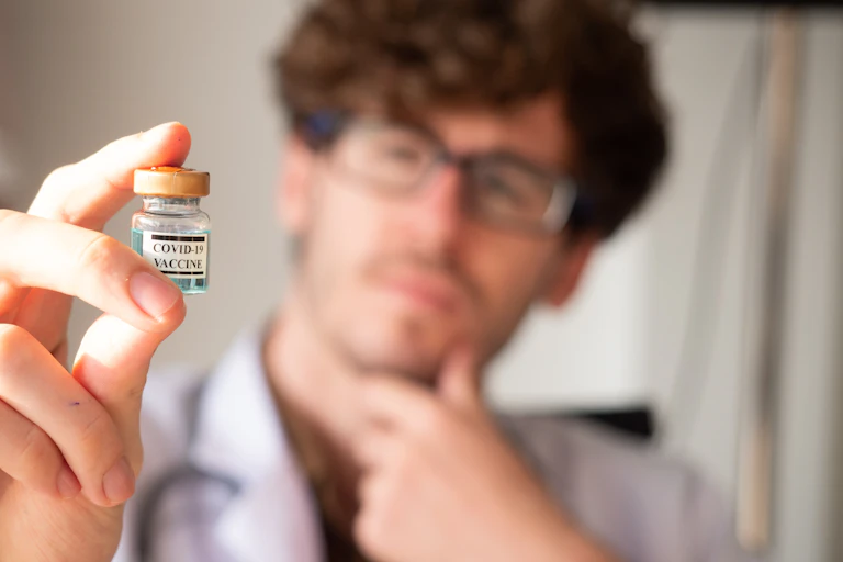 A man looks quizzically at a phial of COVID-19 vaccine.