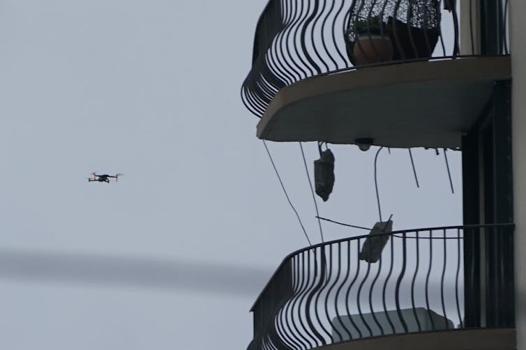 à gauche un drone est en l'air, à droite deux balcons d'une tour d'immeuble