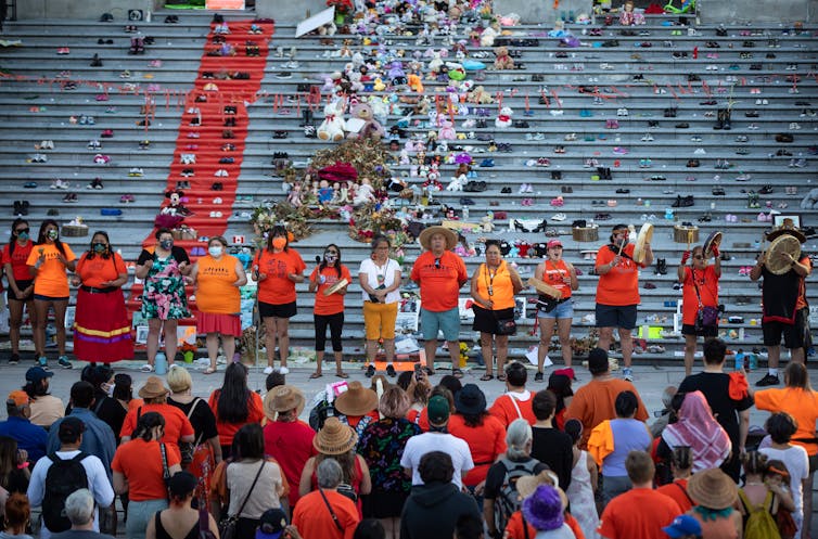 Group of people wearing orange stand in front of steps covered with childrens shoes