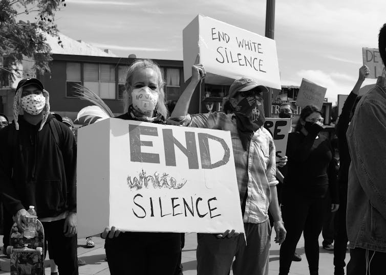 Woman holds a sign that reads 'end white silence'