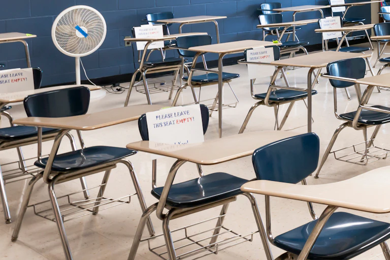 A row of empty classroom seats and a floor fan