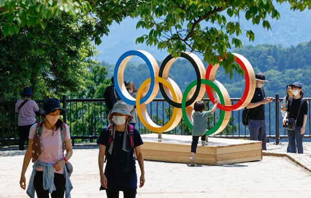 Two tourists wearing masks in front of Olympic Rings