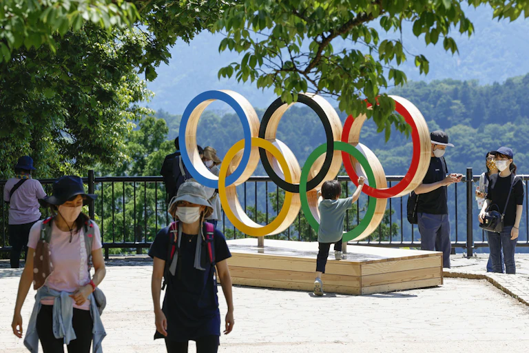 Two tourists wearing masks in front of Olympic Rings