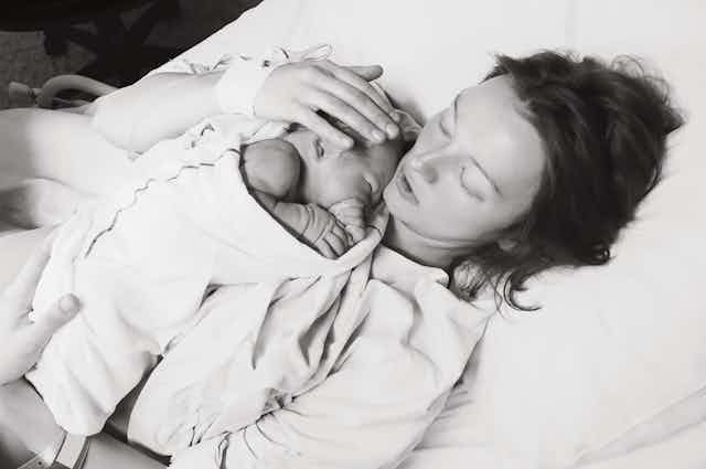 Black and white image of woman lying on a bed with a newborn baby. 