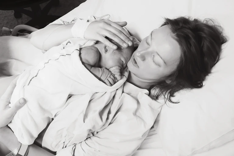 Black and white image of woman lying on a bed with a newborn baby.