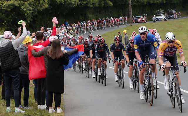 Spectators holding a French flag on the side of the road as the Tour De France riders cycle past
