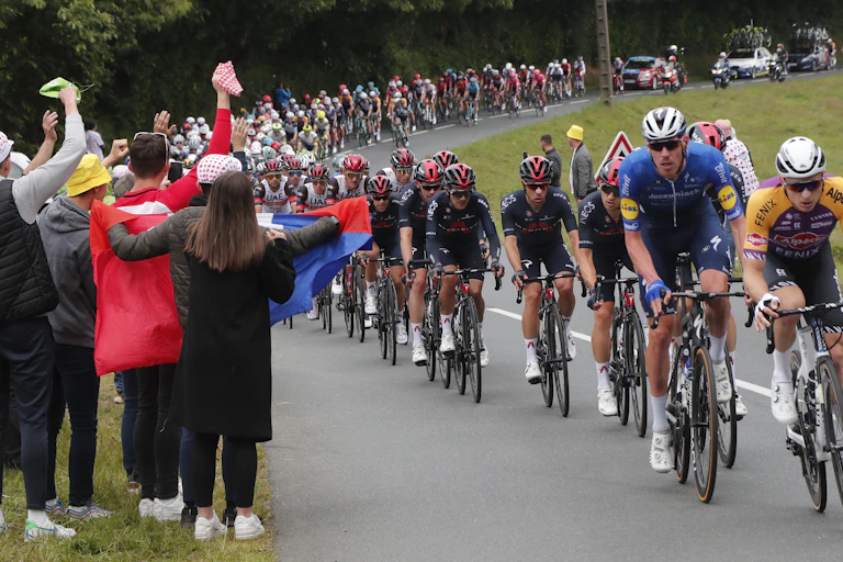 Spectators holding a French flag on the side of the road as the Tour De France riders cycle past