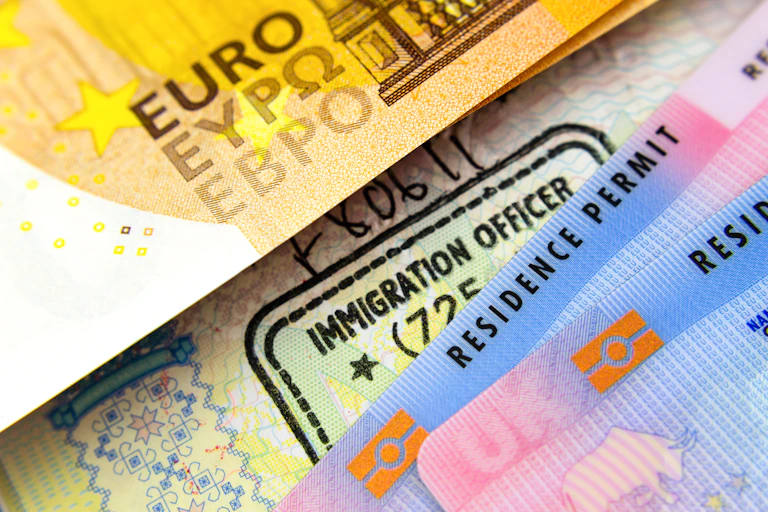 Close up photo of euro notes, a passport stamp, and a UK residence permit