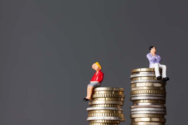A figure of a woman and a figure of a man sit on unequal stacks of coins.