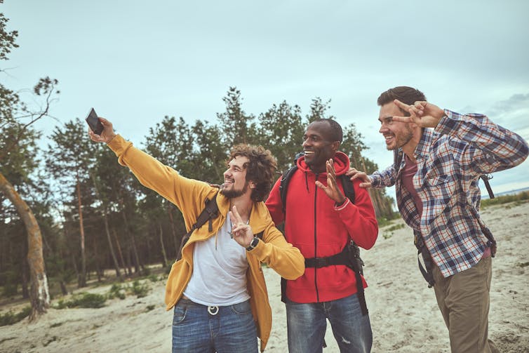Three men pose for a selfie on a beach while hiking.