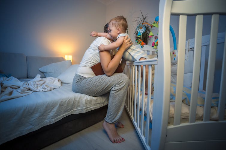 A woman picks up a baby from her bed, in an apartment, in the middle of the night