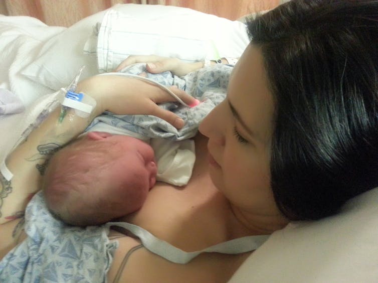 A woman looks at a newborn baby in her arms