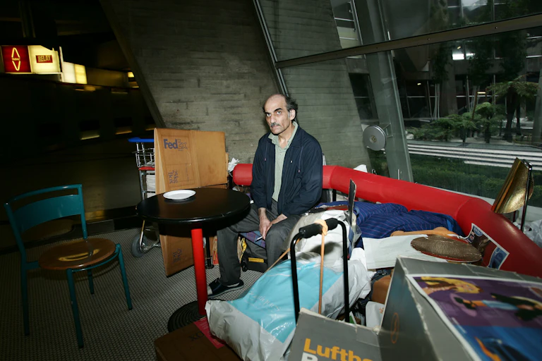 A man sits near his gear on a red bench in an airport terminal.